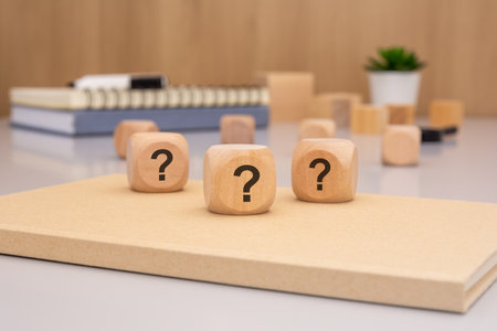 On a desk, three wooden cubes adorned with question marks stand as a powerful symbol of curiosity and inquiryの写真素材