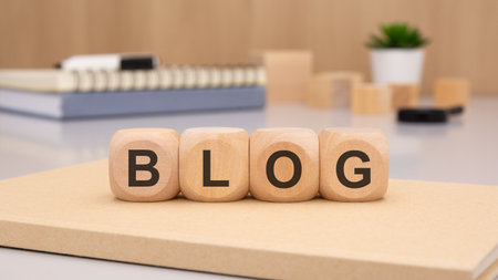 Four wooden cubes with rounded edges spelling BLOG lie on an office desk, symbolizing creativity and content creationの写真素材