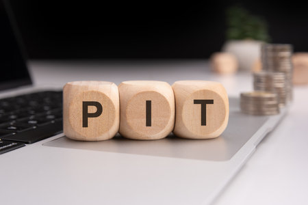 Wooden cubes forming the word 'PIT' on a laptop keyboard, with stacked coins in the background. Represents financial markets, investment, trading, stock exchange, or business strategy concepts.の写真素材