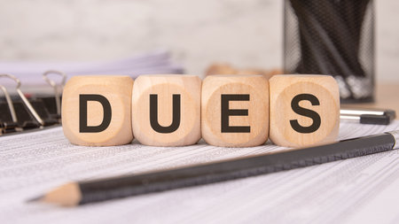 close-up of wooden cubes with the word DUES placed on financial documents, representing payments, or financial obligations. office supplies in the background emphasize a professional setting.の写真素材