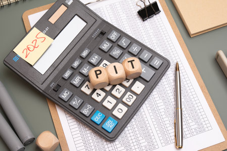 Wooden cubes spelling PIT on a calculator surrounded by a financial spreadsheet, pen, binder clip, and 2025 note, symbolizing tax, finance, and personal income conceptの写真素材