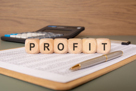 wooden cubes spelling PROFIT on a financial sheet with pen and calculatorの写真素材