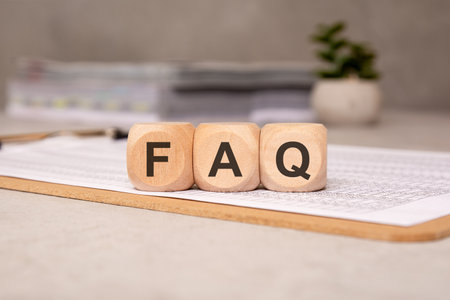 Wooden blocks spelling FAQ (Frequently Asked Questions) on a clipboard with documents, symbolizing help and support sectionの写真素材