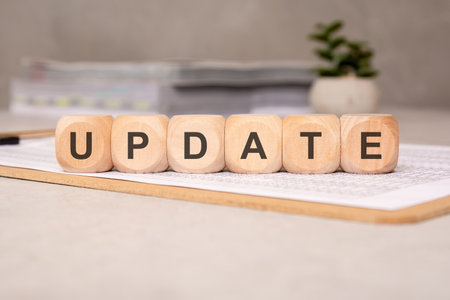 Six wooden cubes spelling the word UPDATE, placed on a clipboard with financial documents, in office settingの写真素材