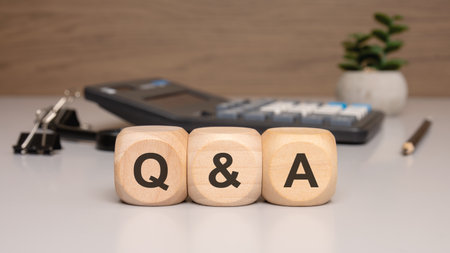Wooden cubes with letters Q and A on desk with calculator, plant, and office supplies
