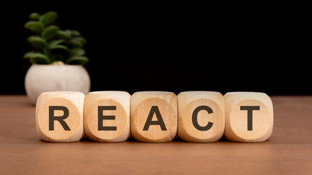 wooden cubes with black letters spelling REACT on brown table with small green plant background