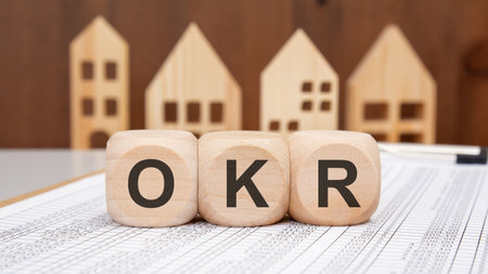 Three wooden cubes with OKR letters placed on spreadsheet, representing objectives and key results in business planning, productivity and performance measurement strategyの写真素材