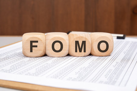Close-up of wooden blocks with the word FOMO on a financial spreadsheet. Concept of investor fear of missing out, finance anxiety, and stock market behaviorの写真素材