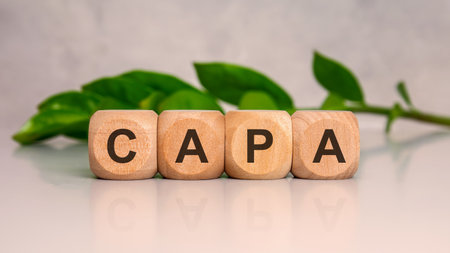 close-up of wooden cubes with the word CAPA on a glossy surface and green leaves in the background. concept for environment, sustainability, or certification.の写真素材