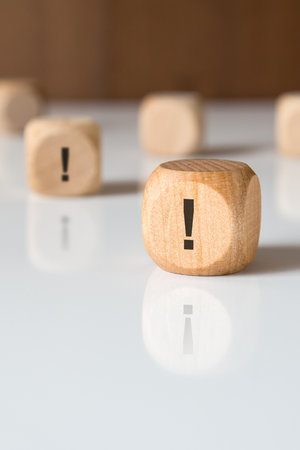 close-up of a wooden cube with an exclamation mark symbol on a white glossy surface. concept of attention, caution, warning, or important information in business or communication.の写真素材