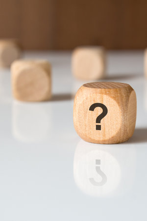 Close-up of a wooden cube with a printed question mark on a glossy surface. Concept for uncertainty, curiosity, problem-solving, or decision-making in business or life.の写真素材