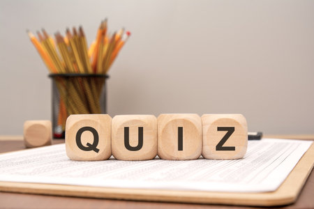 Wooden cubes with the word QUIZ arranged on a clipboard with printed sheets, pencils in a holder in the background. Concept of education, testing, knowledge assessment, or online learning.の写真素材