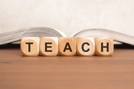 Wooden cubes forming word TEACH placed on desk with open book in background, symbolizing education, learning, teaching, and knowledge sharingの写真素材