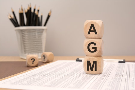 Wooden cubes spelling AGM on office supplies, symbolizing annual general meeting and corporate governanceの写真素材