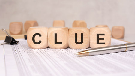 Four natural wood blocks marked CLUE sit on printed papers with a pen nearby, suggesting the process of discovery, investigation, critical thinking, and finding meaningful insights.の写真素材