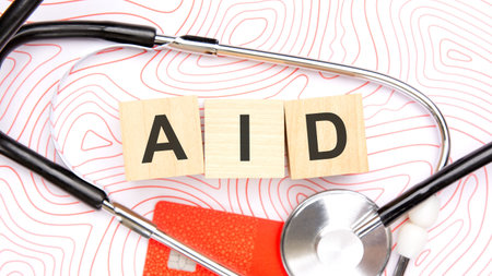 Top view flat lay of wooden cubes spelling the word AID inside a medical stethoscope loop with a credit card. Concept of paid medical services, health insurance, financial support for treatment, and humanitarian aid. White background with red abstract lines.の写真素材