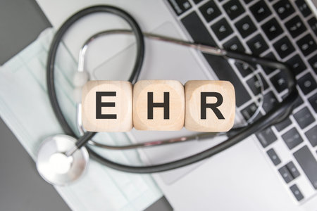 Top view flat lay of wooden blocks spelling EHR (Electronic Health Record) resting on a medical...