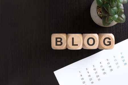 Top view flat lay of wooden blocks spelling the word BLOG, arranged with a monthly calendar and a...
