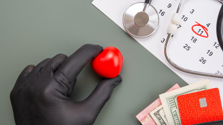 Top view flat lay of a hand in a black nitrile glove holding a red heart. Composition includes a...