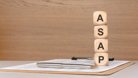 Vertical stack of wooden toy blocks spelling ASAP on a desk with a financial report and a pen....