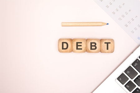 Top view flat lay of wooden toy blocks spelling the word DEBT on a bright neutral background....