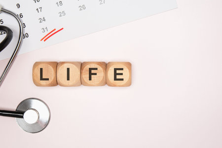 Top view flat lay of wooden toy blocks spelling the word LIFE. Composition includes a medical...