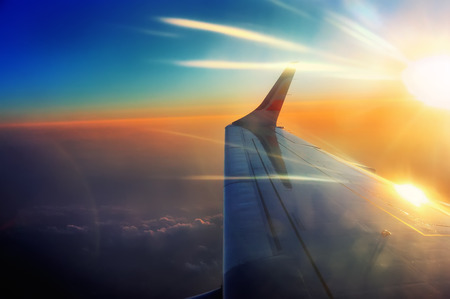 porthole view wing of the airplane in flight in sunrise beamsの写真素材