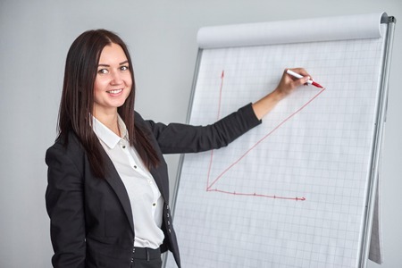 Smiling woman in black jacket writing on large paper chart with marker in office and presents the diagramの写真素材