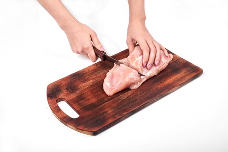 Cutting raw turkey meat with a kitchen knife on a cutting board isolated on white backgroundの写真素材