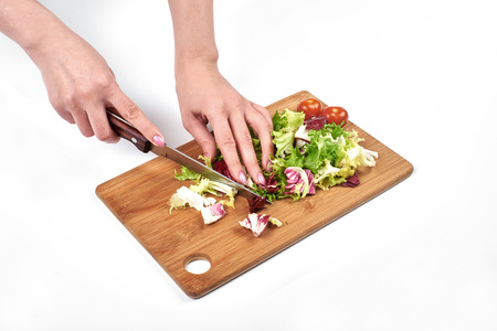 Closeup of woman cooks hands slicing salad and vegetables on a wooden board, isolated on white backgroundの写真素材
