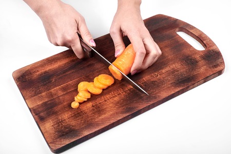 Closeup of woman cooks hands, slicing the carrot on a wooden board, isolated on white backgroundの写真素材