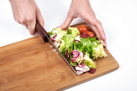 Closeup of woman hands slicing salad and vegetables on a wooden board, isolated on white background, copy spaceの写真素材