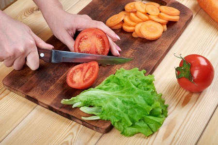 close up of female hand cutting tomato on cutting board at home, cooking, food and home conceptの写真素材