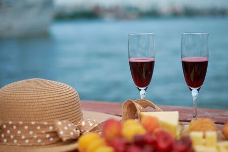 Two glasses of red wine, served outdoor with fruits and beautiful blue ocean view.の写真素材