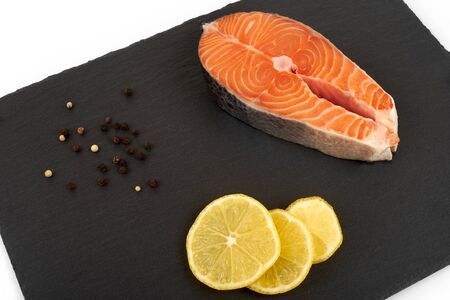 Salmon steak raw fish with a lemon prepared for cooking. Top view on black slate table.の写真素材