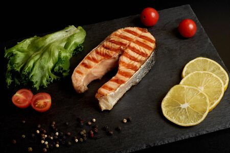 Grilled salmon steak with a lemon, tomatoes and salad on a slate plate.の写真素材