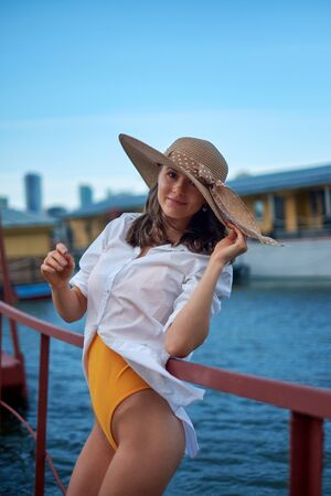 Beautiful girl in a hat , posing on a pier, on a background of waterの写真素材