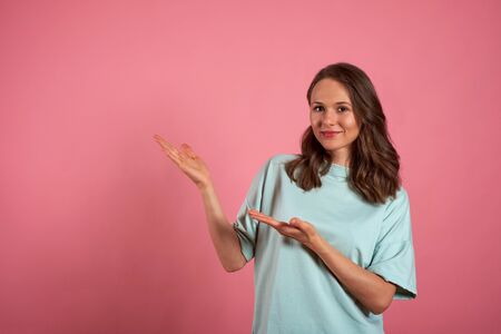 Young woman looks at the camera and pointing somewhere to the side on a pink backgroundの写真素材