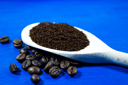 Ground Coffee in wooden spoon on blue background