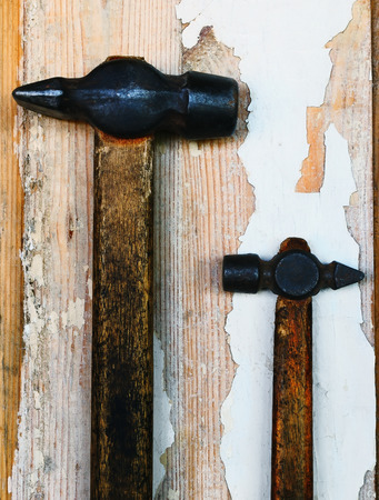 Two old hammer of different sizes lie on the wooden board with traces of old white paintの写真素材