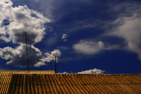 The roofs of the houses with the television antenna in the background of a picturesque cloudy sky on a sunny summer dayの写真素材