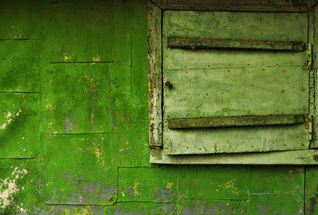 Old building - closed window and part of the wall, covered with a green cracked paint