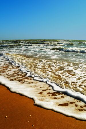 Sea wave run through the golden sand on the beach on a warm sunny cloudless day of summer closeupの写真素材