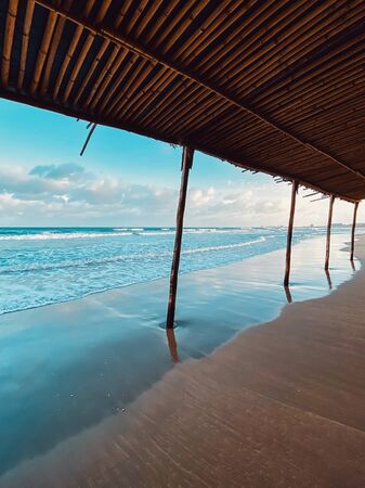 Seascape, sea view from under the bamboo roof. Waves at sea, sea tide, sandy shore. Beautiful clouds in the sky. Traveling in Asia. Bamboo buildings on the beach.の写真素材