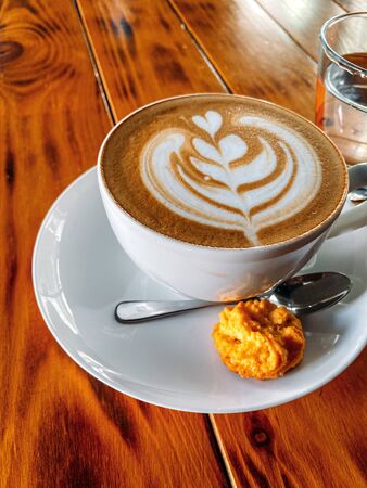 Cup of cappuccino standing on a wooden table, White cup on a plate with cookies, Texture of old wood panels, brown texture background, color, natural wood, place for text, free space. Texture of old wood panels, brown texture background, color, natural wood, place for text, free space.の写真素材