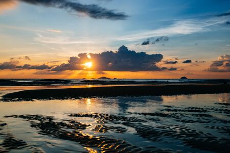 Sea, sunrise, clouds letting in the sun's rays reflection of the sun on the shore, blue sky