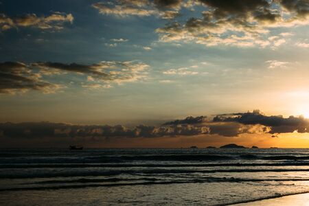 Sea, sunrise, clouds letting in the sun's rays reflection of the sun on the shore, blue skyの写真素材