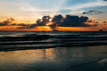 Sea, sunrise, clouds letting in the sun's rays reflection of the sun on the shore, blue sky