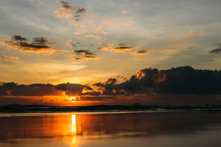Sea, sunrise, clouds letting in the sun's rays reflection of the sun on the shore, blue sky