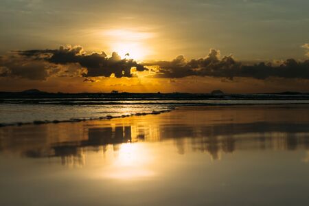 Sea, sunrise, clouds letting in the sun's rays reflection of the sun on the shore, blue skyの写真素材